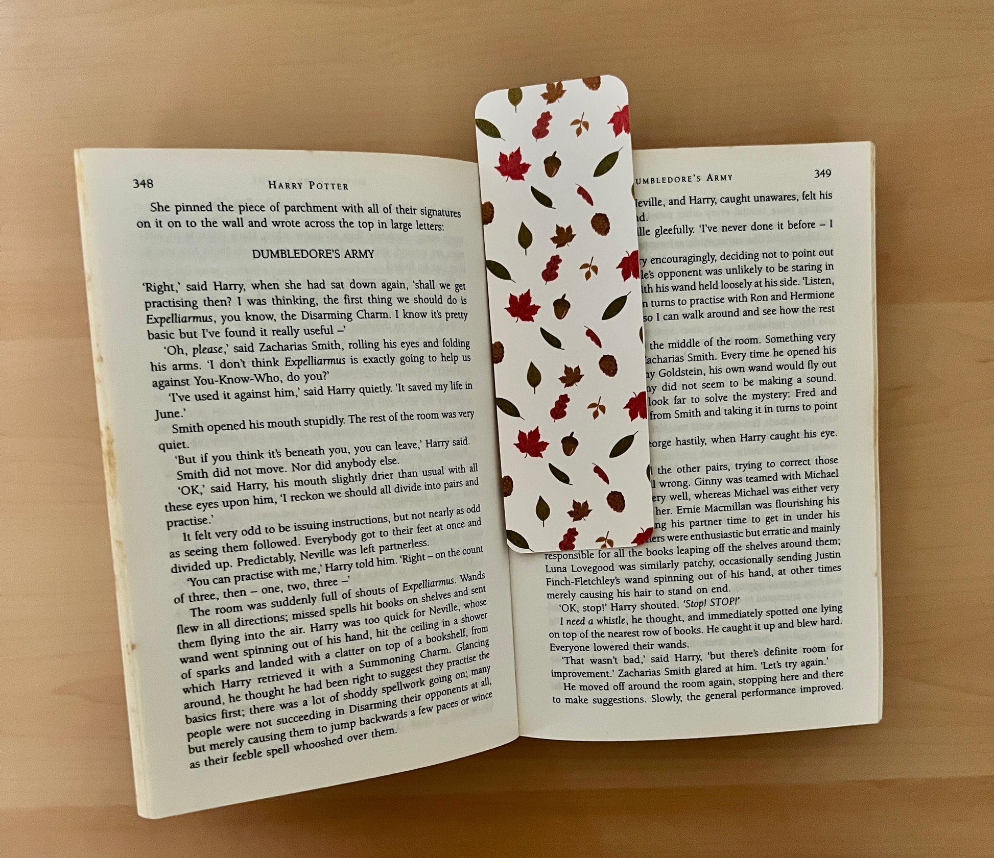 Open book with a decorative bookmark featuring autumn leaves on a wooden surface