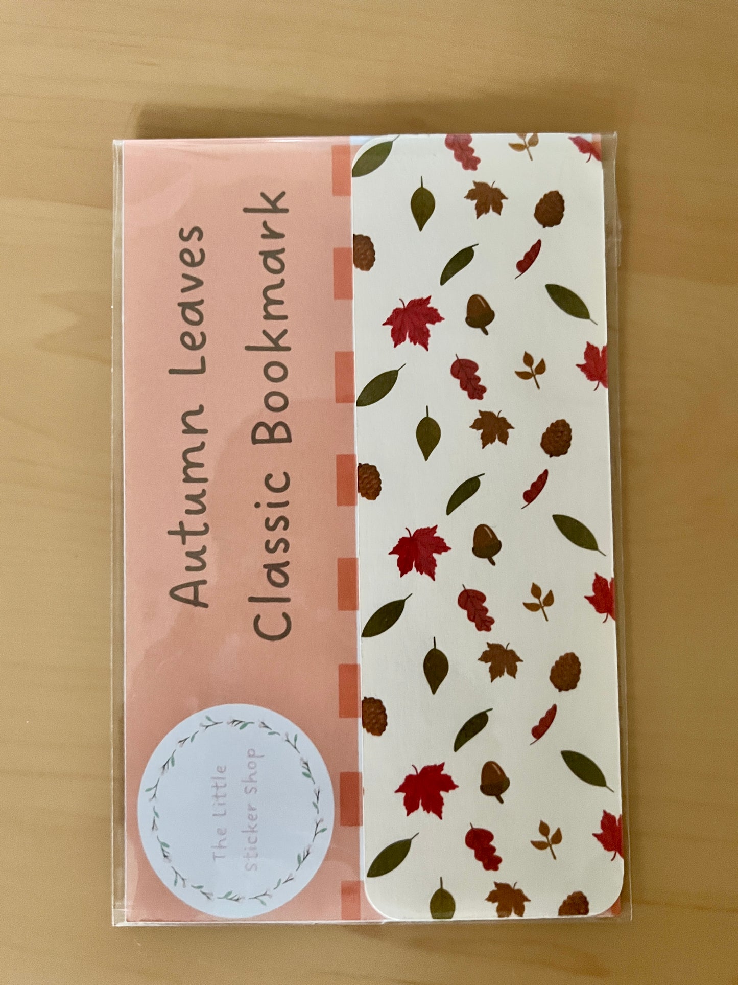 Packaging of 'Autumn Leaves Classic Bookmark' with a orange and white design on a wooden surface.