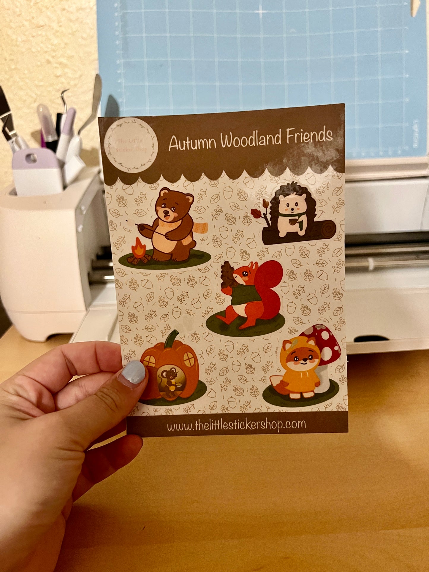 Sticker sheet with 5 cute character animals - a bear roasting a marshmallow over a campfire, a hedgehog drinking a hot drink on a log - a squirrel carrying a mountain of acorns, a fox in a raincoat, and a mouse in a pumpkin house.