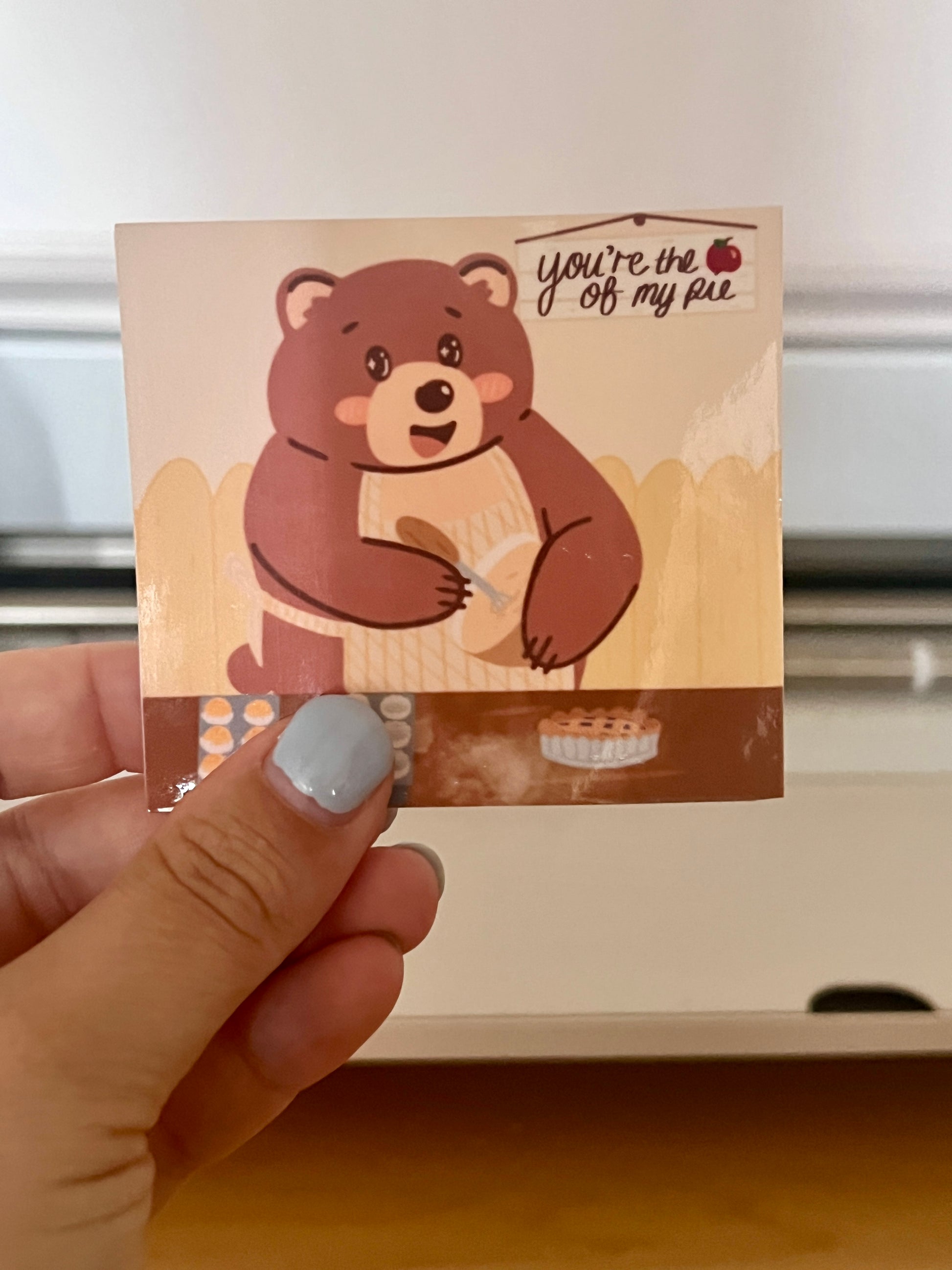 Die-cut sticker being held, of an Autumn Bear baking baked goods. 