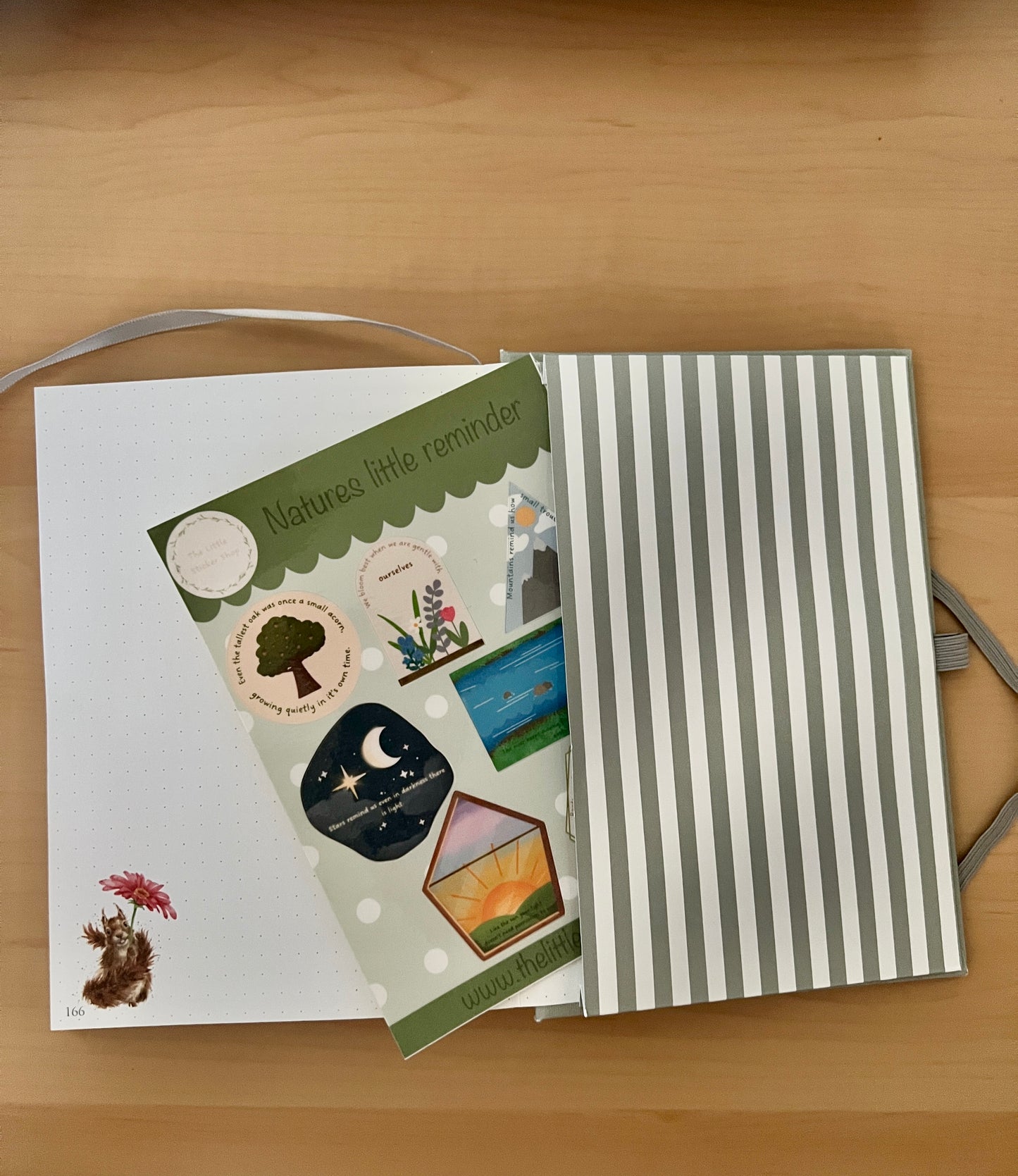 Notebook with a striped cover and a sticker sheet with nature-themed illustrations on a wooden surface.