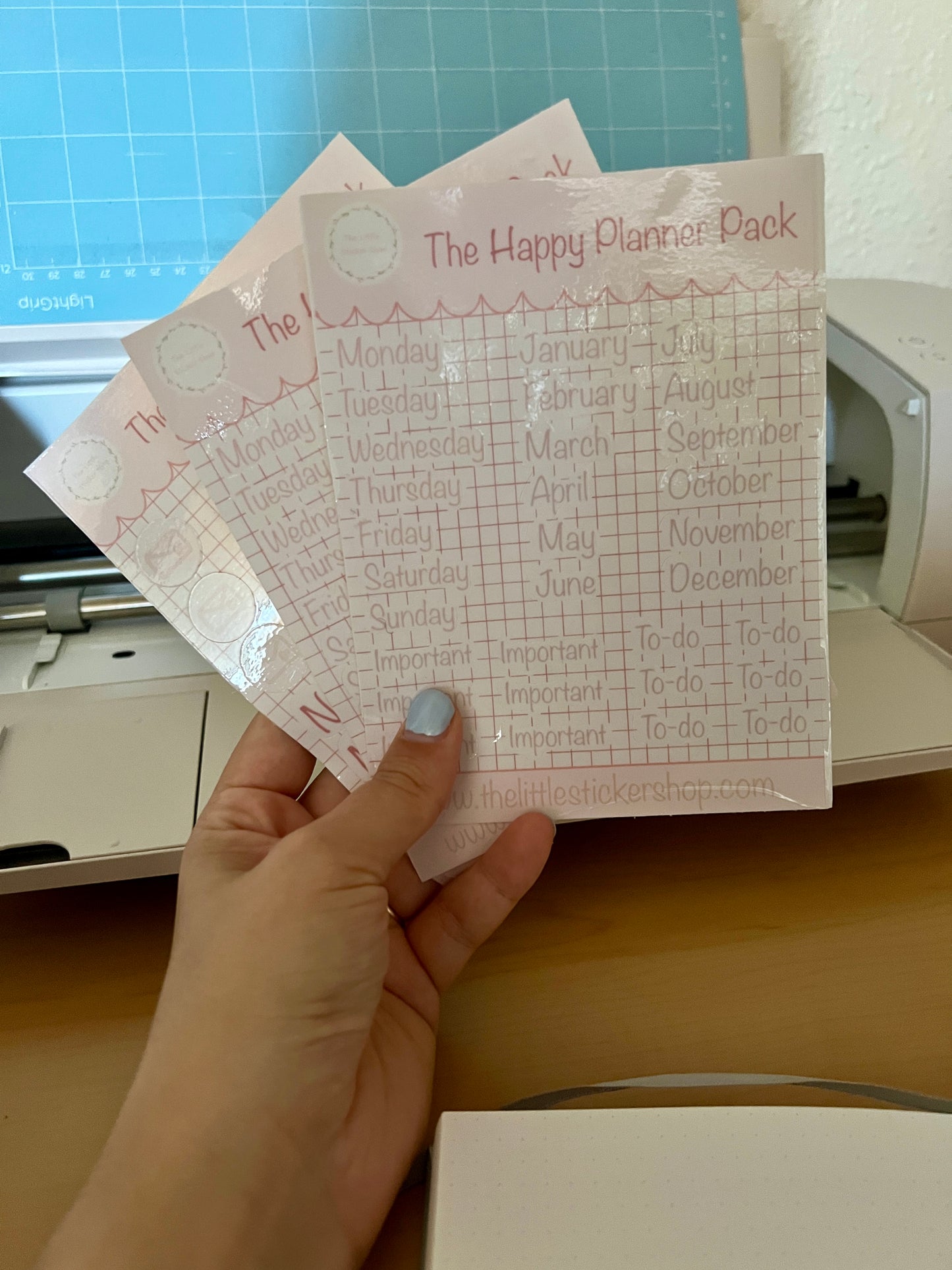 Hand holding a planner sheet with 'The Happy Planner Pack' branding on a cutting mat.