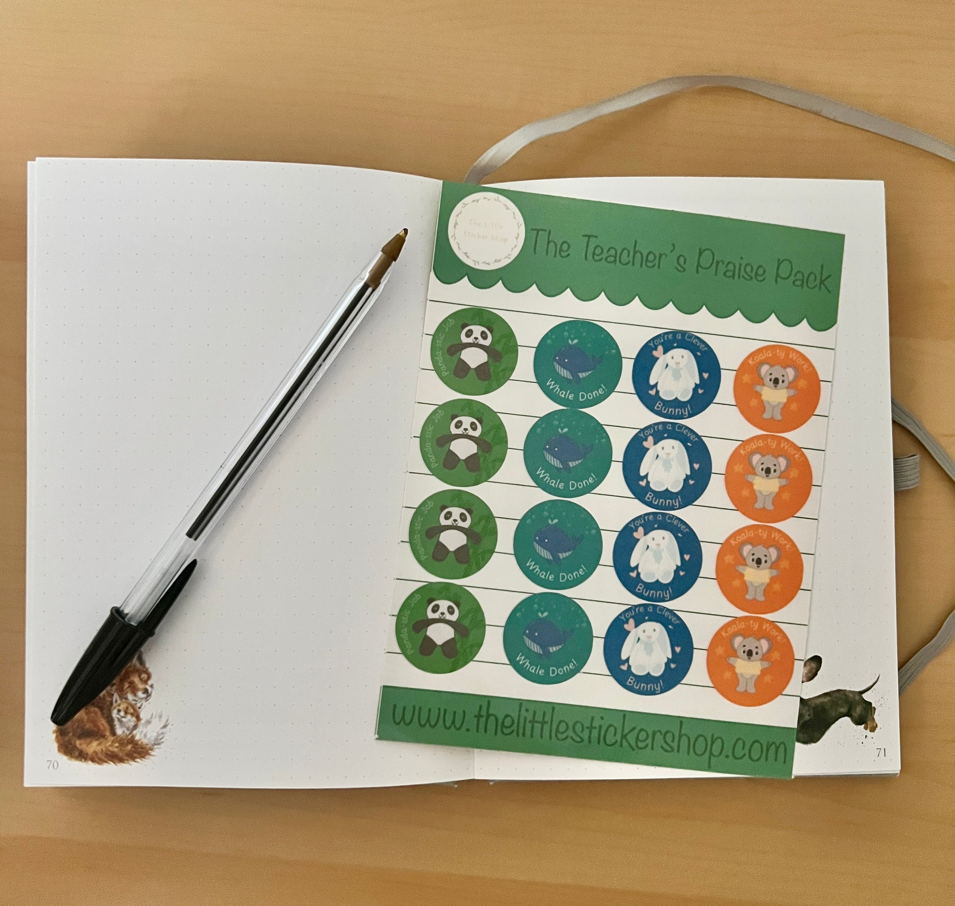 Open book with a sheet of stickers titled 'The Teacher's Praise Pack' on a wooden surface.