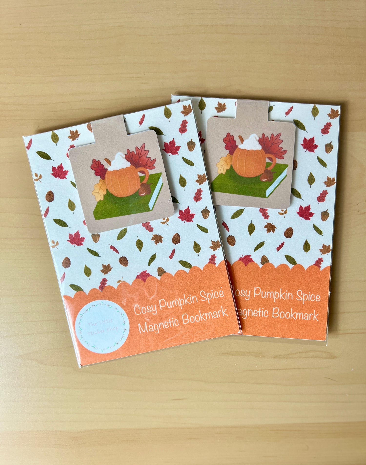 Two 'Cosy Pumpkin Spice' magnetic bookmarks on a wooden surface