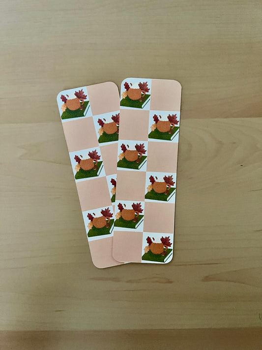 2 card bookmarks arranged on a wooden surface with illustrated pumpkin mug onto of a book with a chequered beige background. 