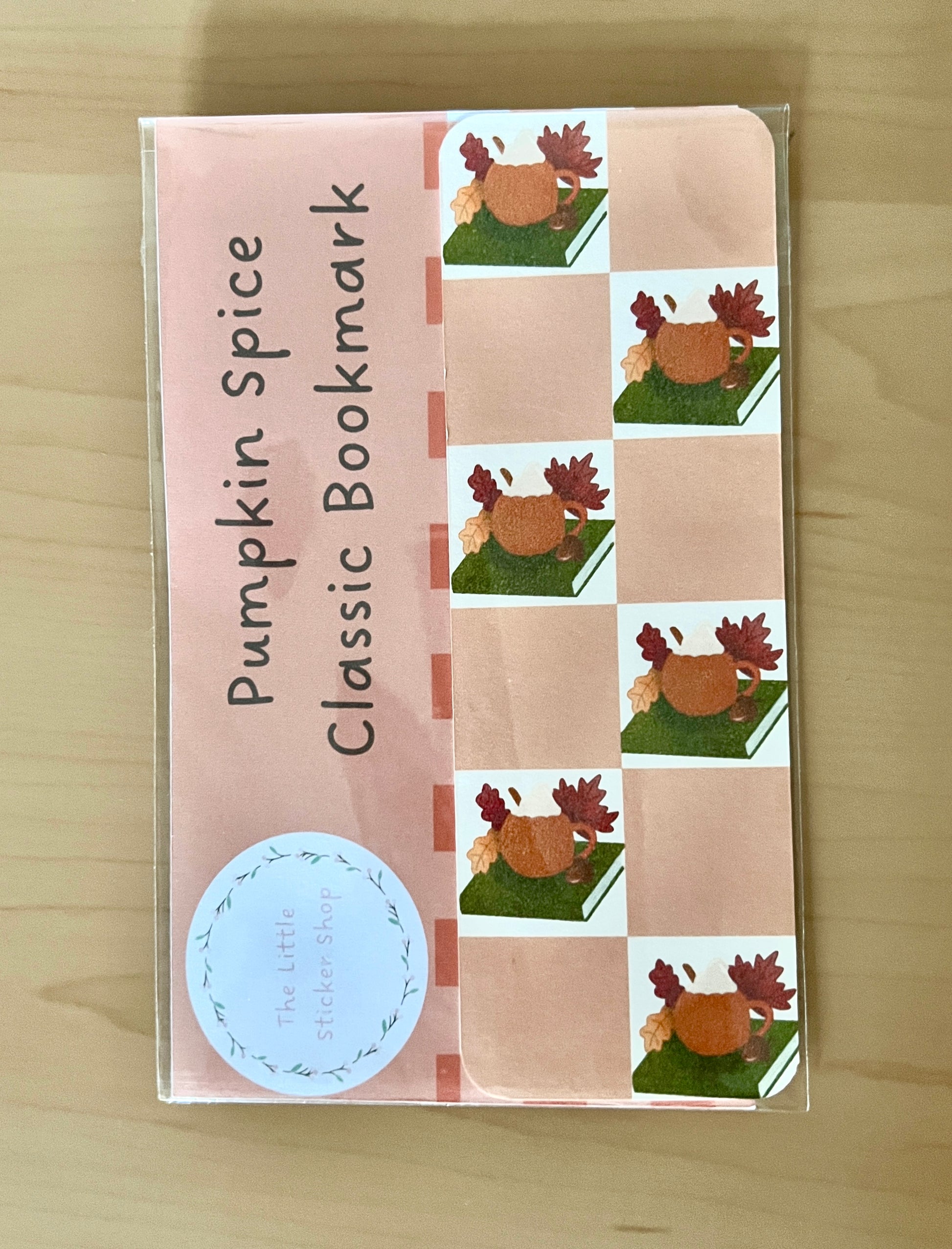 Pumpkin Spice Classic Bookmark packaging with cartoon pumpkin cup on a book on a beige chequered background